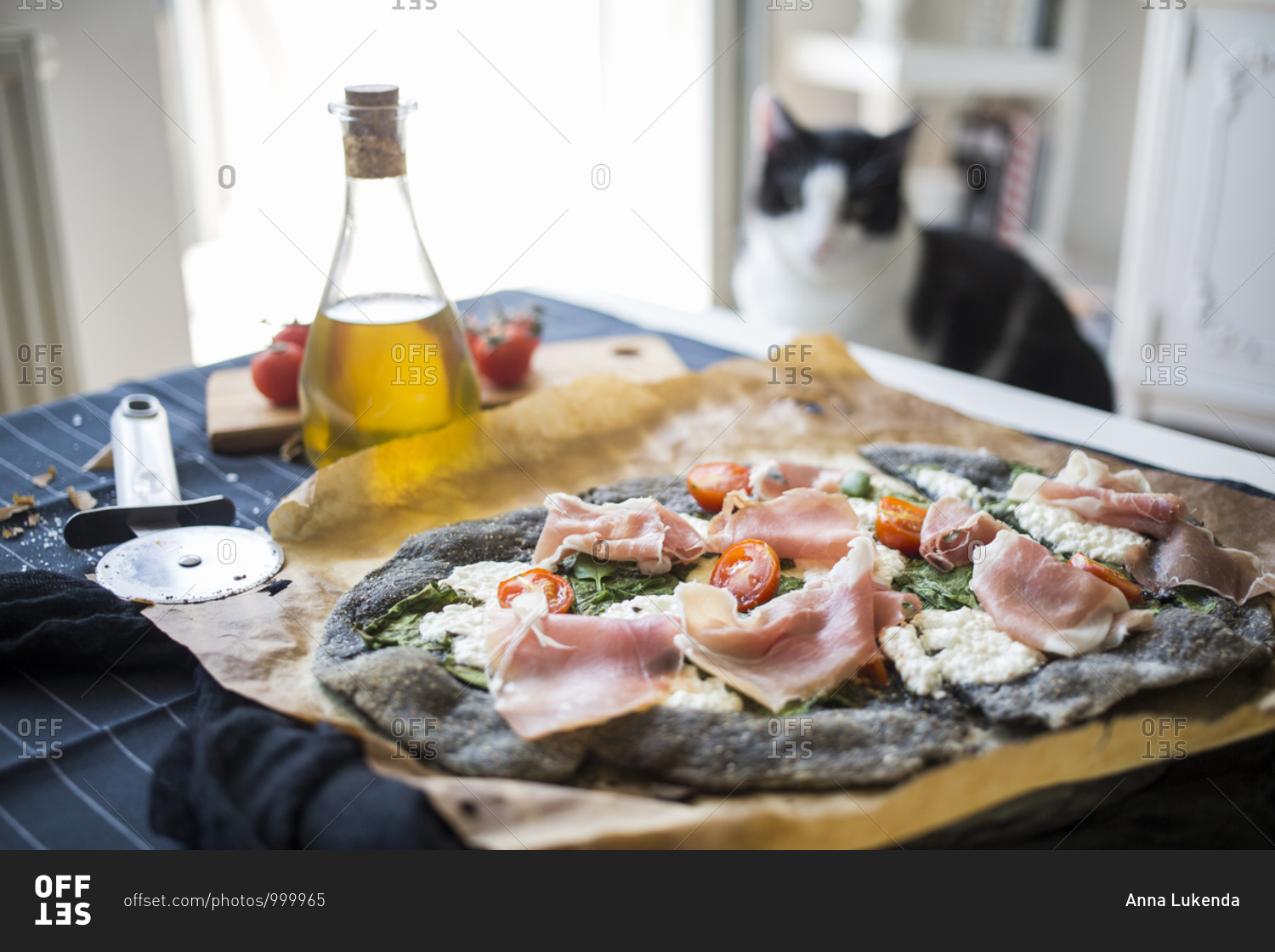 Cat overlooking a black pizza with spinach, prosciutto, tomatoes and homemade goat cheese