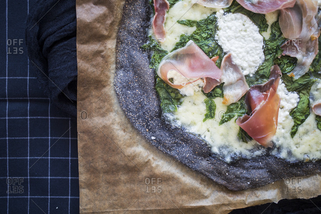 Close up of black pizza with spinach, prosciutto and homemade goat cheese