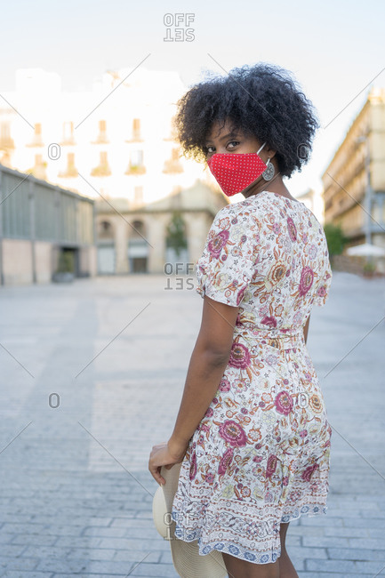 A young African-American woman wearing a medical mask turns to face the camera in a square