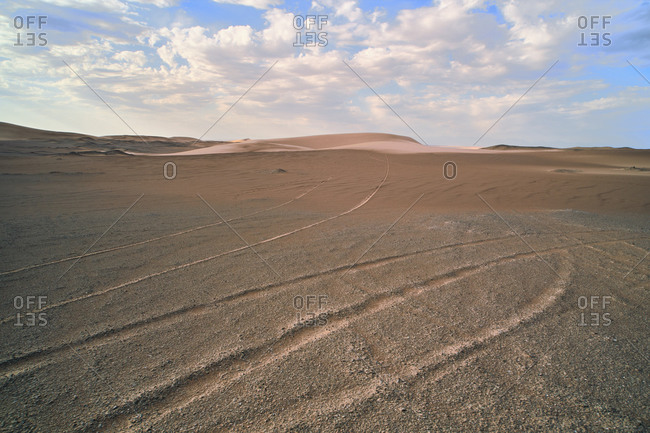 Spectacular view of desert with sandy hills and traces on dry surface with loose texture under serene sky with low clouds in daylight