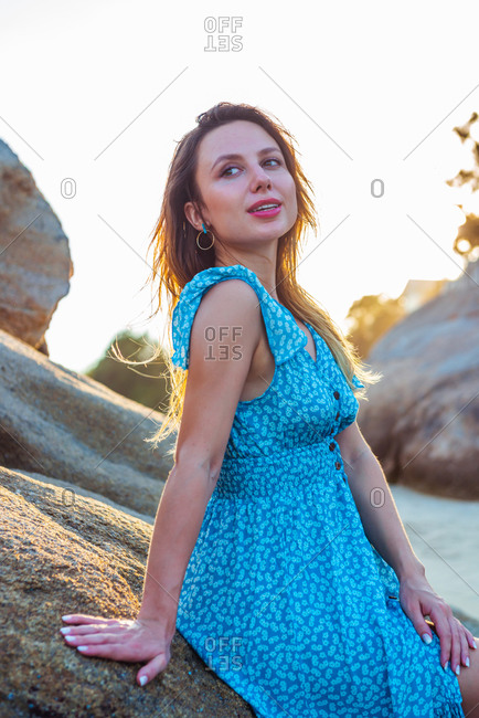 Low angle of woman traveler in summer dress posing on rough rock near sea during summer holidays