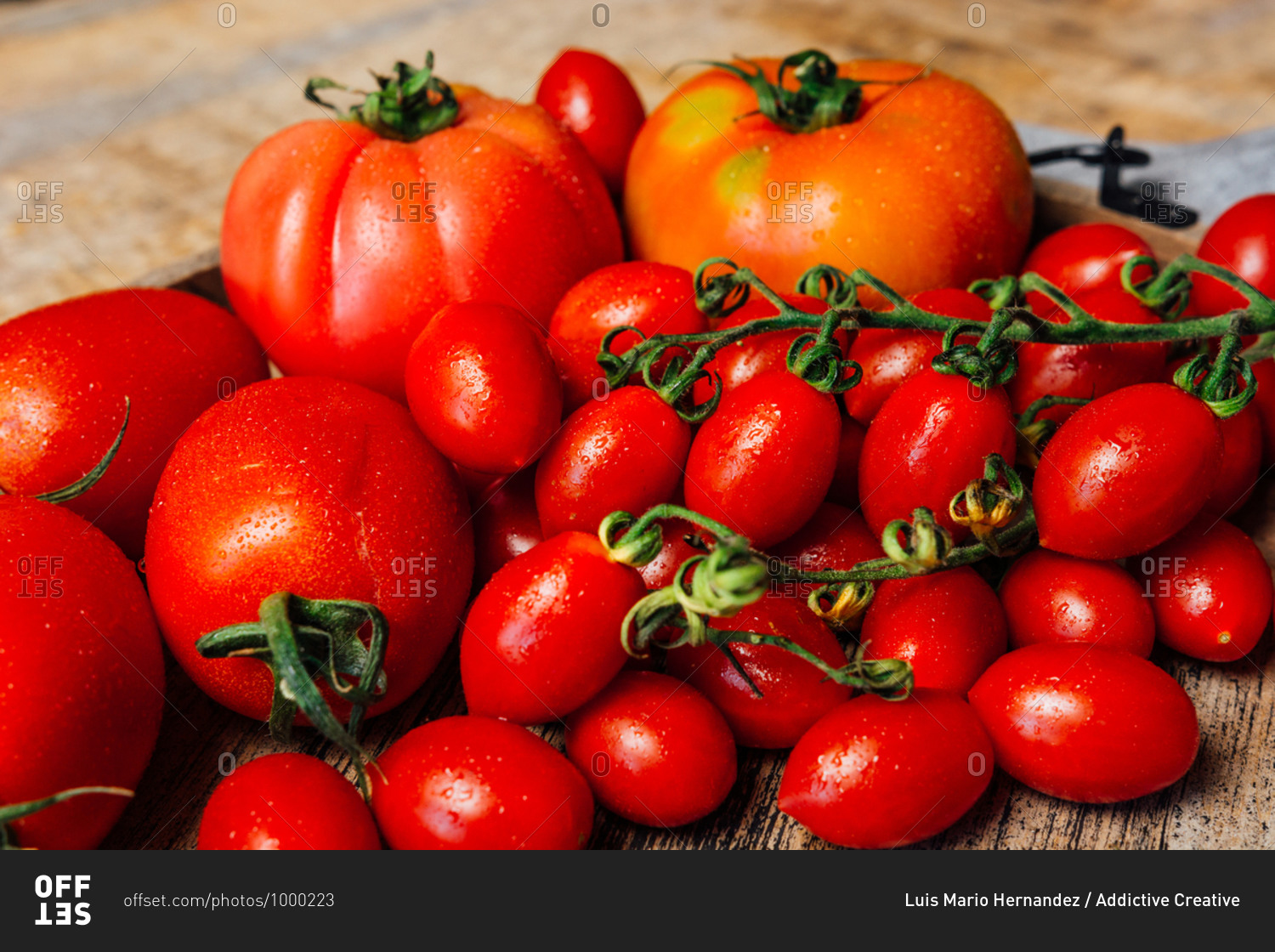 Top view of various types of fresh ripe red tomatoes on wooden tray arranged on rustic wooden table with cloth