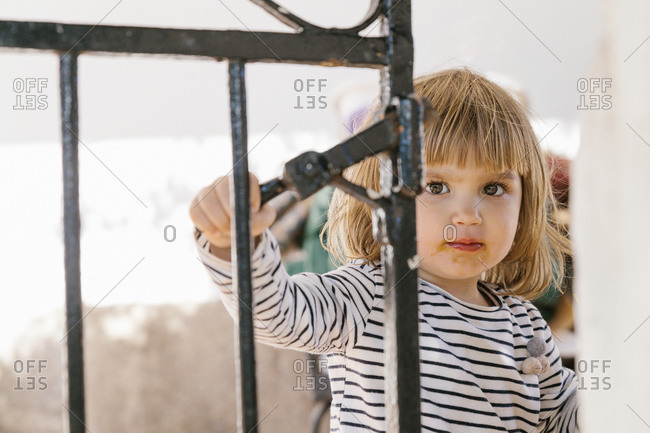 Cute little kid with dirty mouth standing in backyard in summer and looking at camera