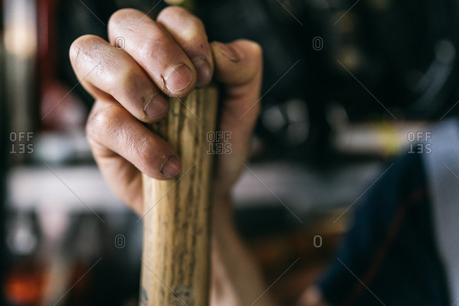 Crop anonymous male employee with dirty nails holding hatchet with wooden handle and smooth surface while working in workshop in daylight