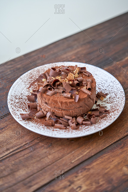 Closeup of palatable chocolate cheesecake sprinkled with cocoa powder and decorated with chocolate shavings served on white plate