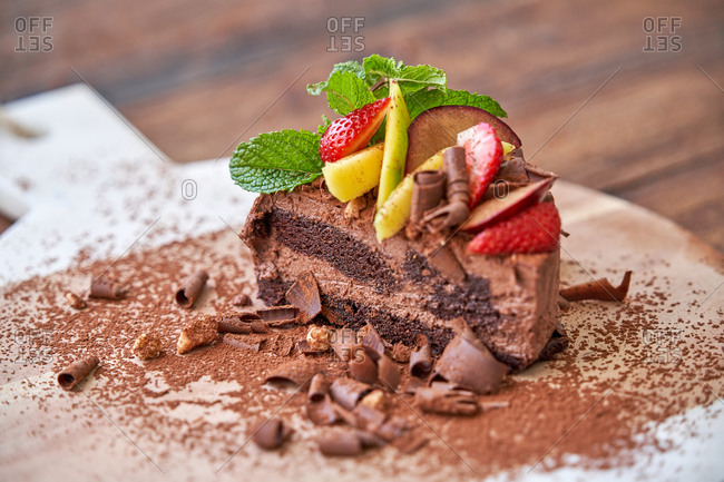 Delectable halved chocolate mousse cake with garnished with fresh mint leaves and fruits with berries served on wooden board on table