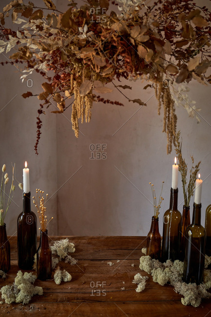 Bunch of dried flowers hanging over wooden table with burning candles in glass bottles
