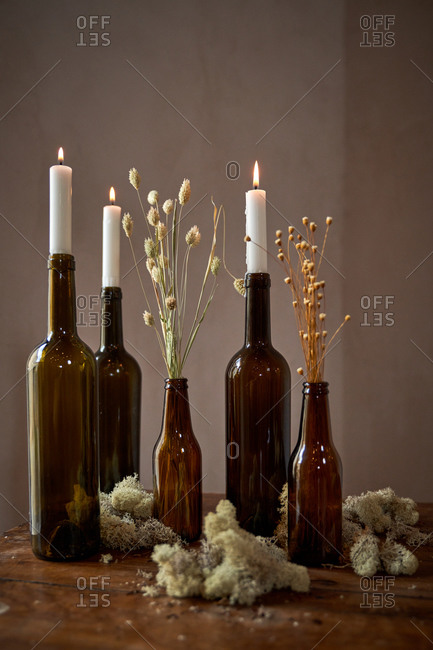 Wooden table with burning candles in glass bottles with dry flowers