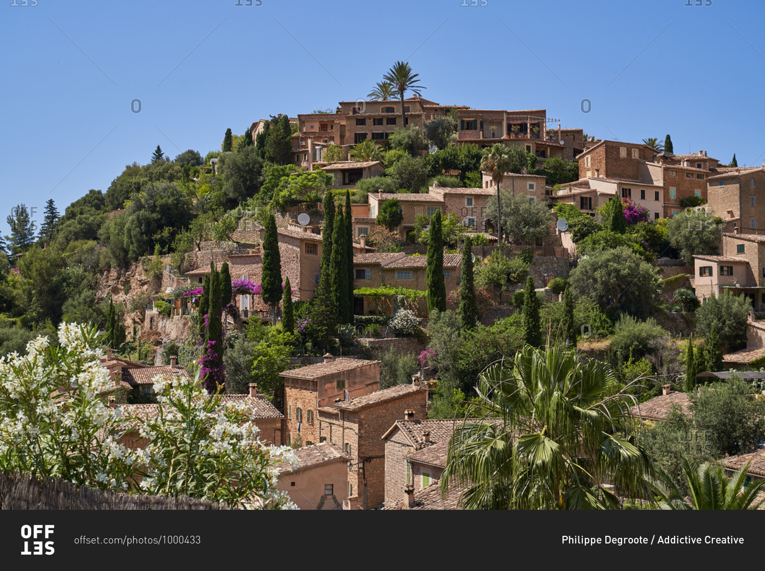 Picturesque view of ancient settlement with small stone houses located on green hill against cloudless blue sky in sunny summer day