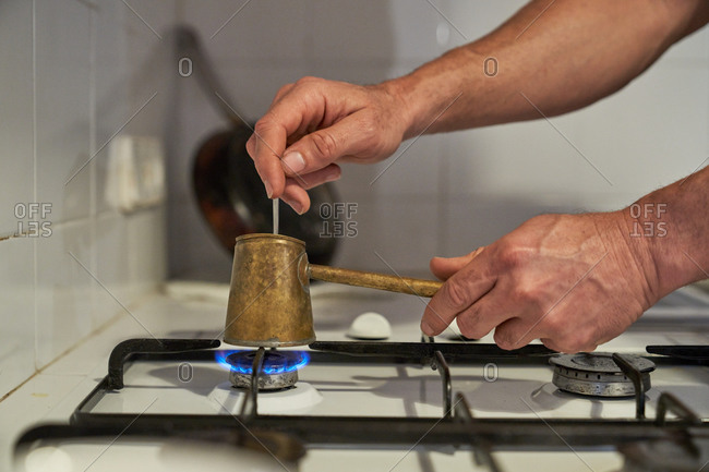 Side view of crop anonymous person standing at stove at home and preparing aromatic coffee in cezve