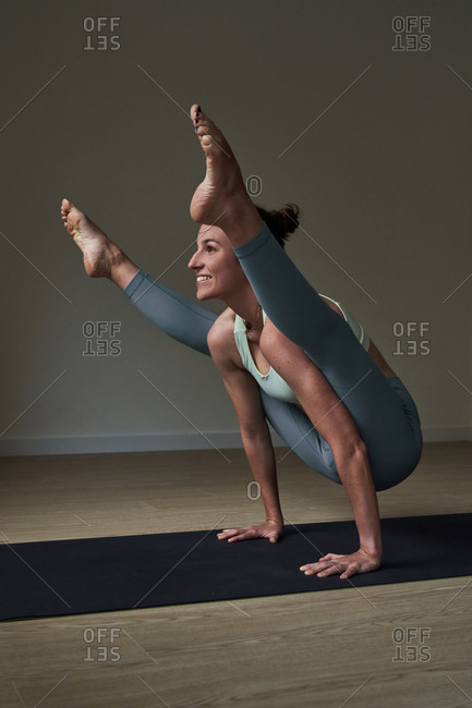 Side view of happy strong young female athlete in leggings balancing on arms while performing Firefly asana during yoga practice