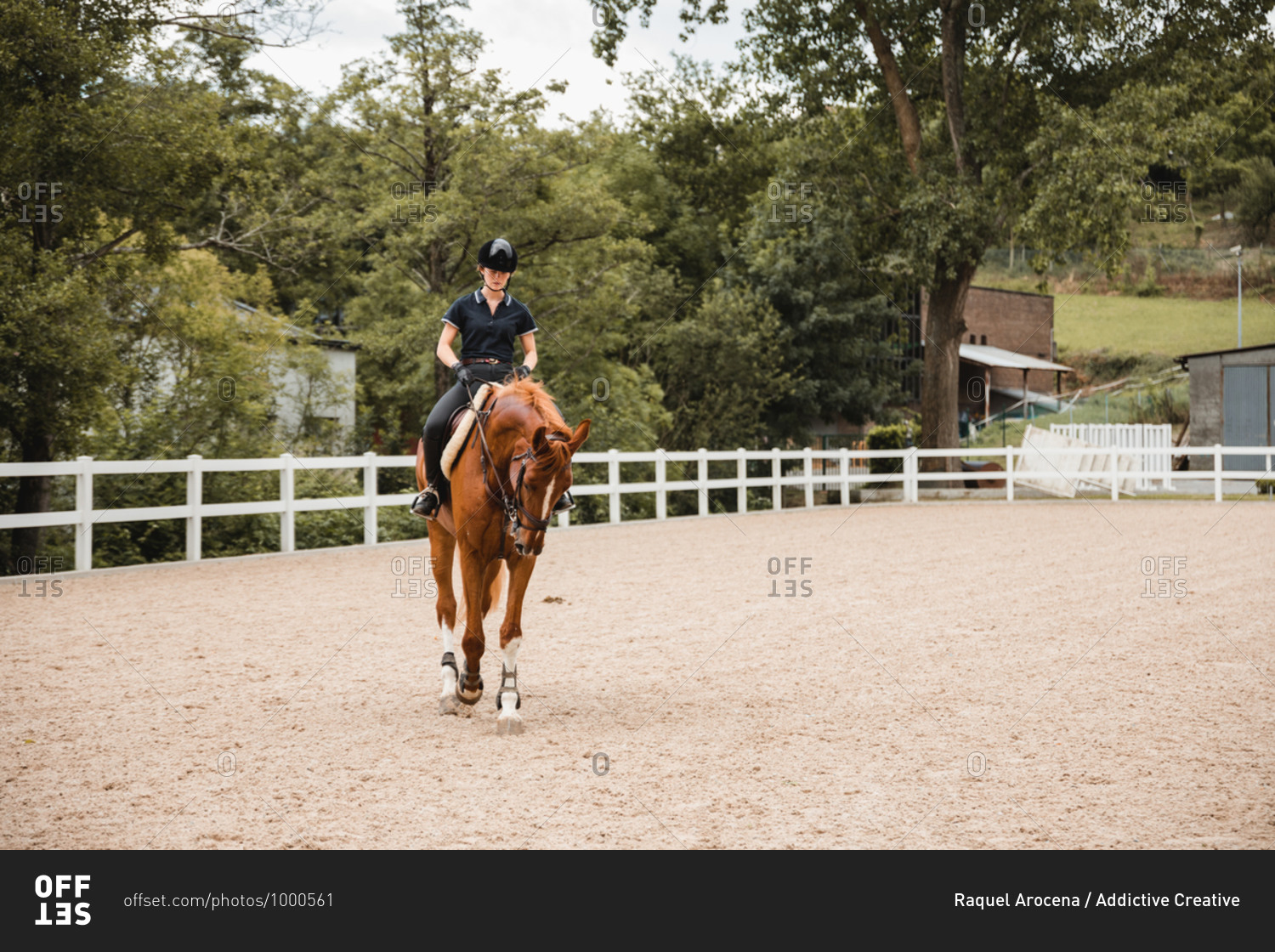 Female equestrian in uniform riding chestnut horse on sand\
arena during dressage on cloudy day stock photo - OFFSET