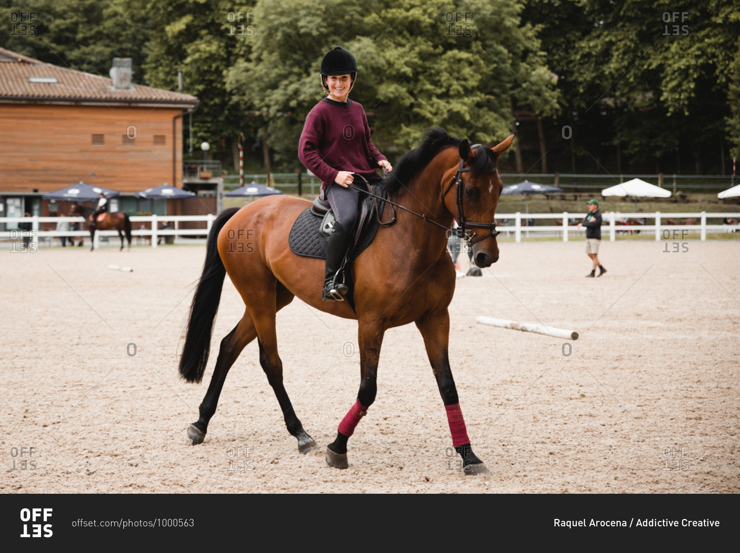 Smiley female equestrian in uniform riding chestnut horse on\
sand arena during dressage looking at camera stock photo -\
OFFSET