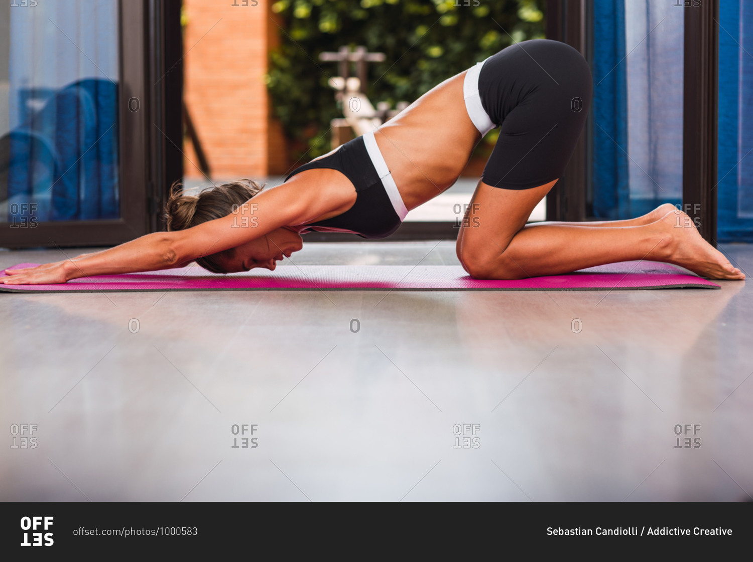 Side view of slender barefoot female in sportswear stretching back while practicing yoga on pink mat on floor in apartment