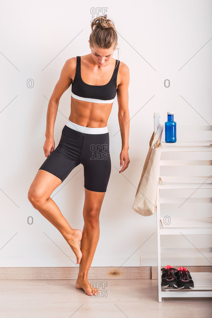 Full body of slim female in activewear standing barefoot in gym