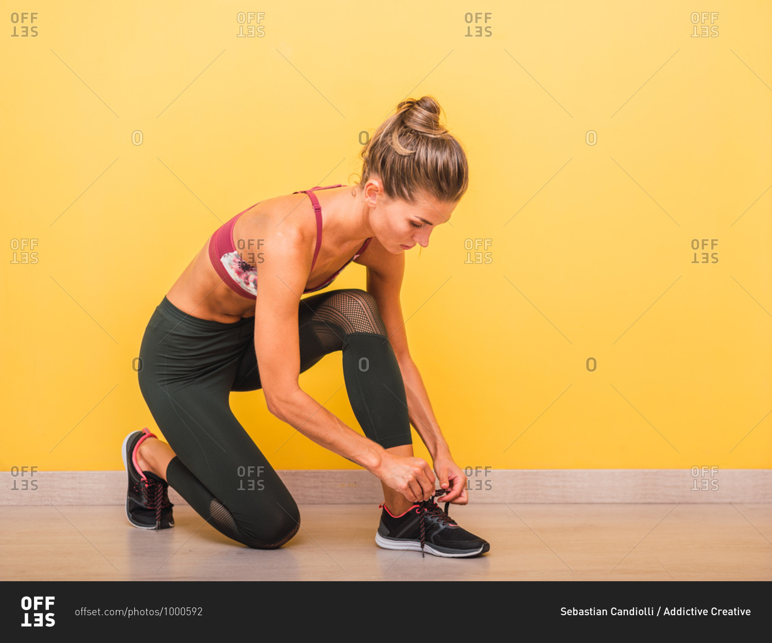 Side view of confident sportswoman in bra and leggings tying shoelaces on sneakers before training in modern gym
