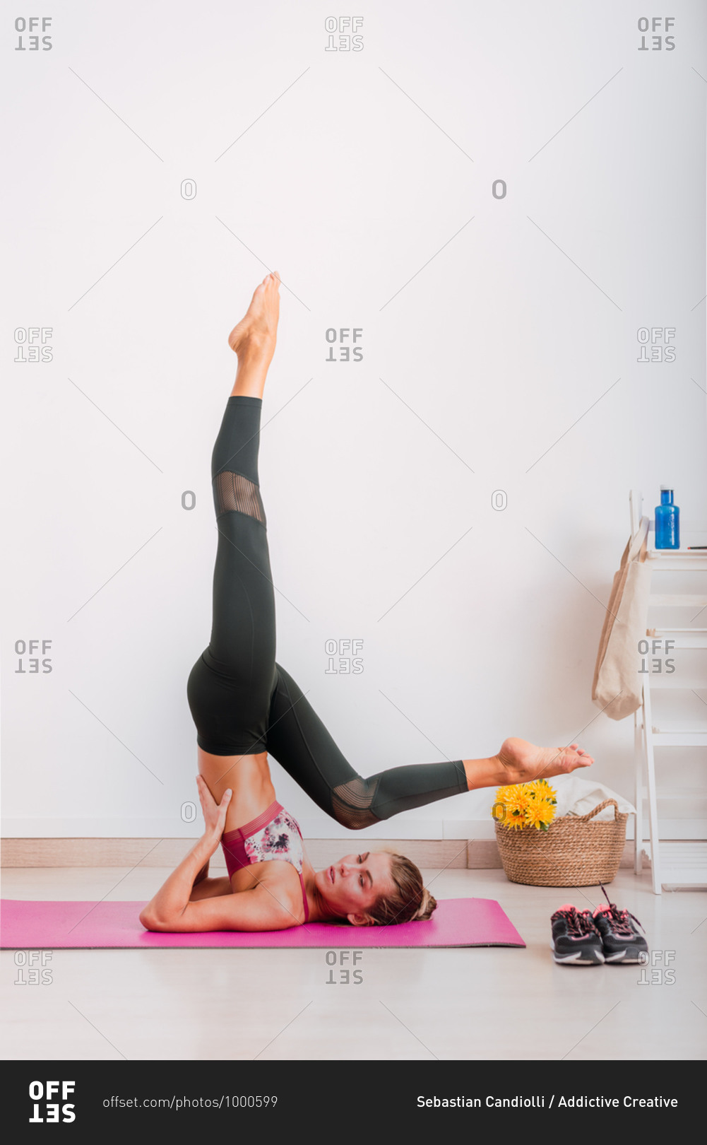 Side view of slender barefoot female in sportswear representing Supported Shoulder Stand pose while practicing yoga on mat on parquet in apartment