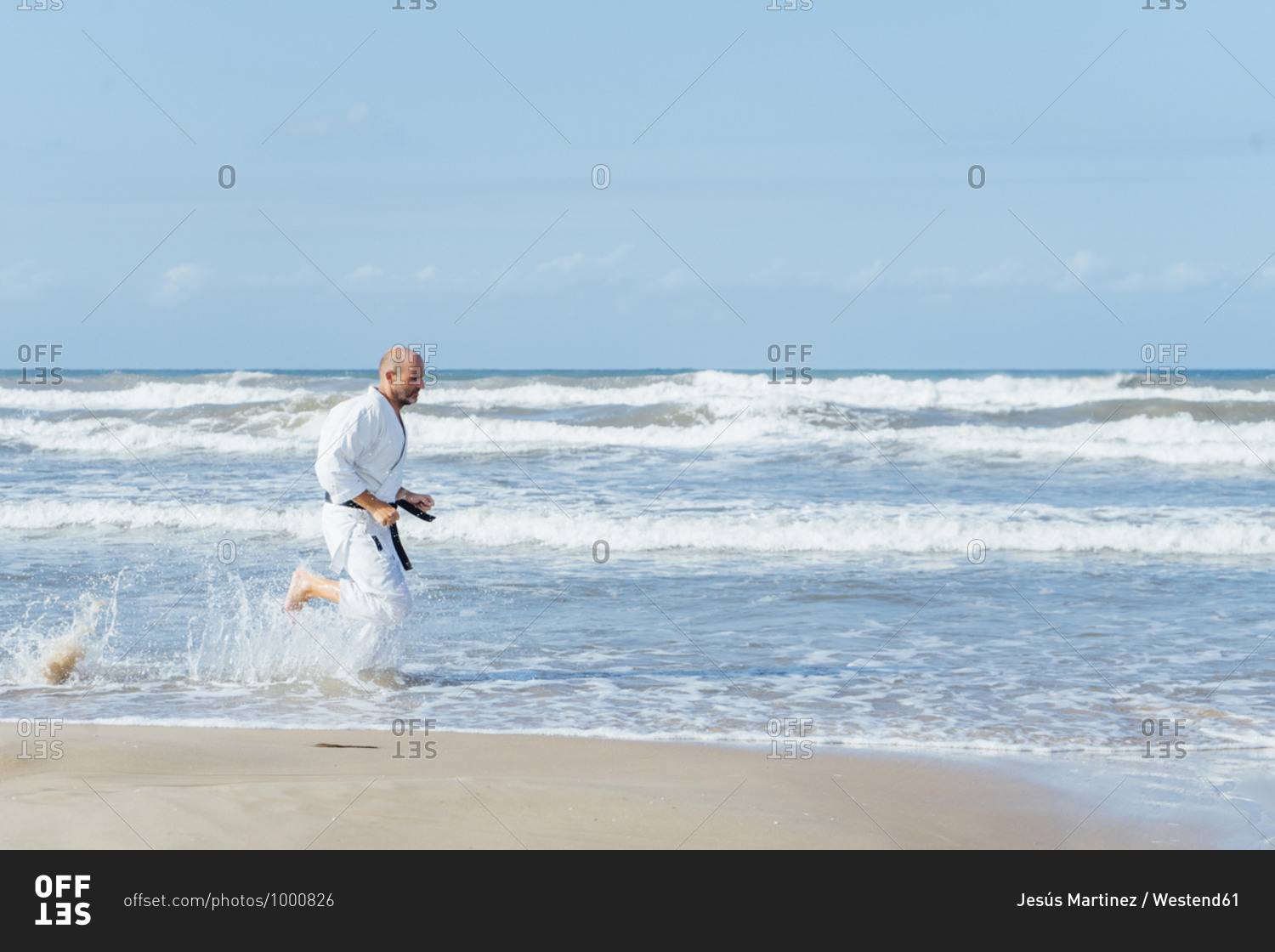 Mature man wearing karate gi running at beach against sky during sunny day