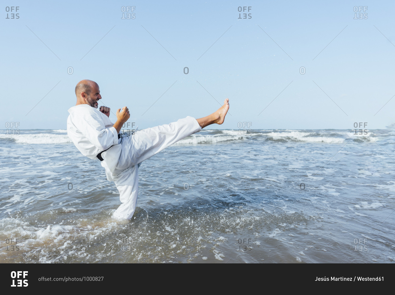 Mature man kicking while practicing karate in sea against clear sky