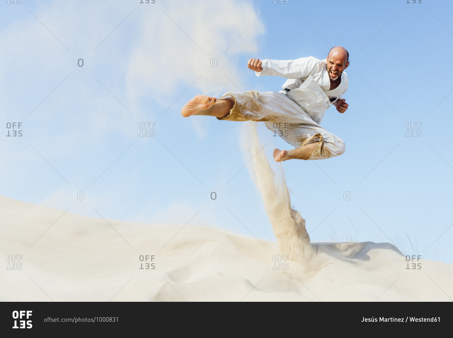 Mature man jumping while practicing karate on sand at beach against sky