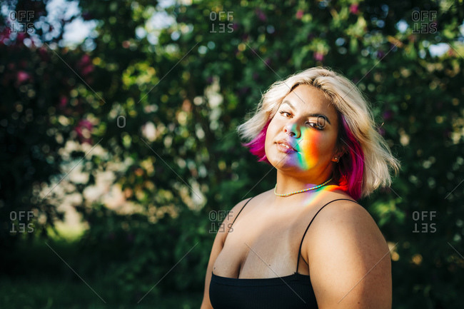 Plus size woman with rainbow lights falling on her face in park