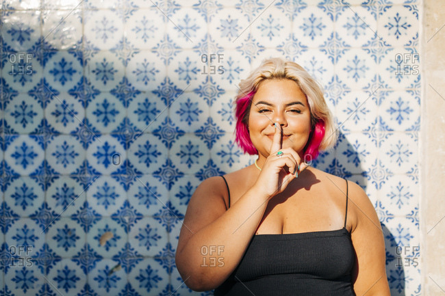 Woman showing silence sign with finger on lips against wall