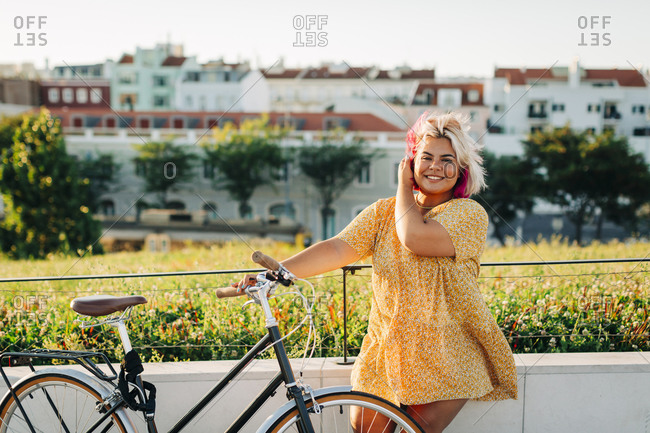 Happy plus size woman with bicycle leaning on park fence