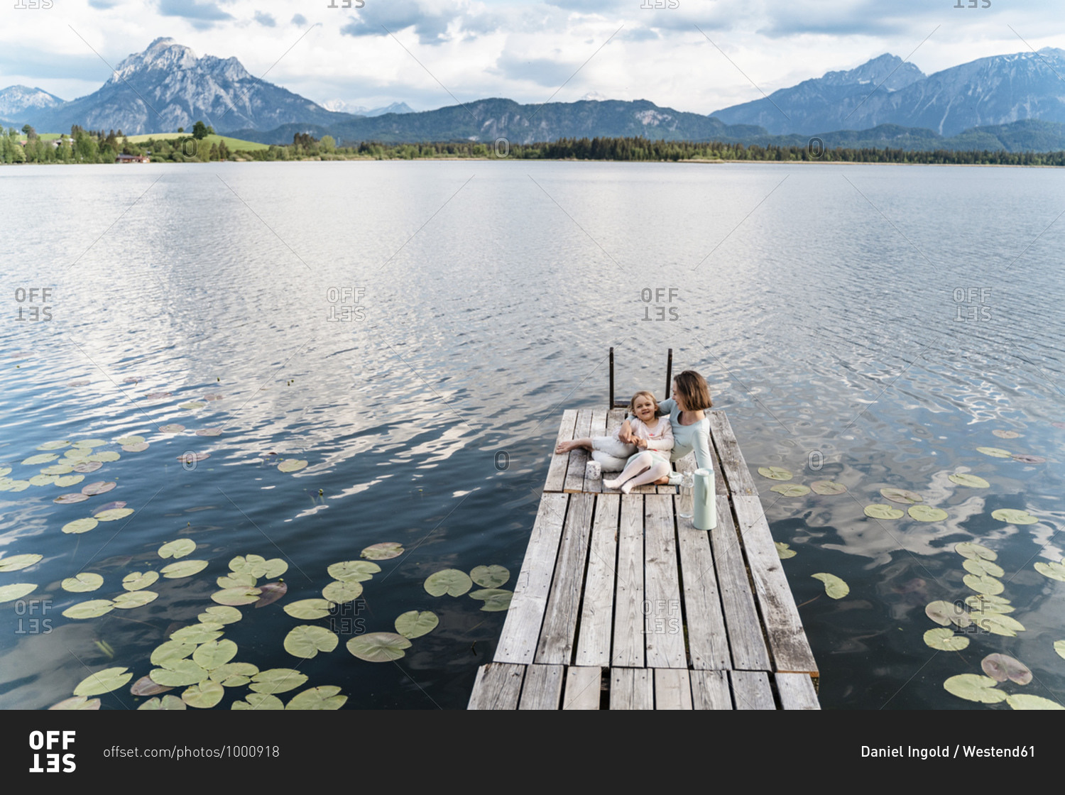 Mid adult woman and daughter sitting on jetty over lake against sky