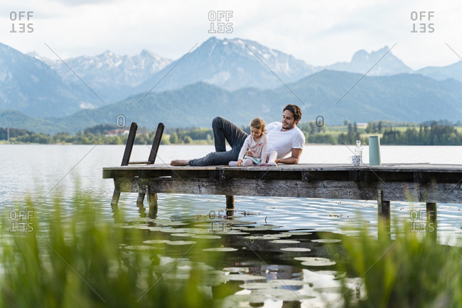 Father with daughter relaxing on jetty over lake against mountains