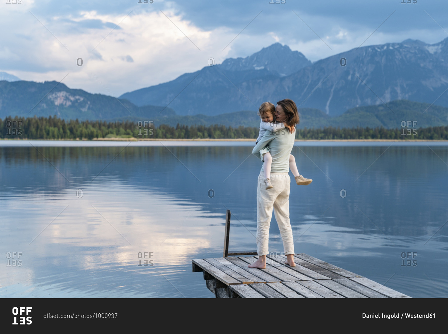 Happy mother carrying daughter while standing on jetty over lake against mountain