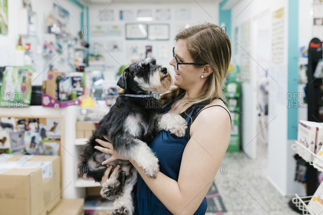 Happy woman carrying schnauzer while standing in pet salon