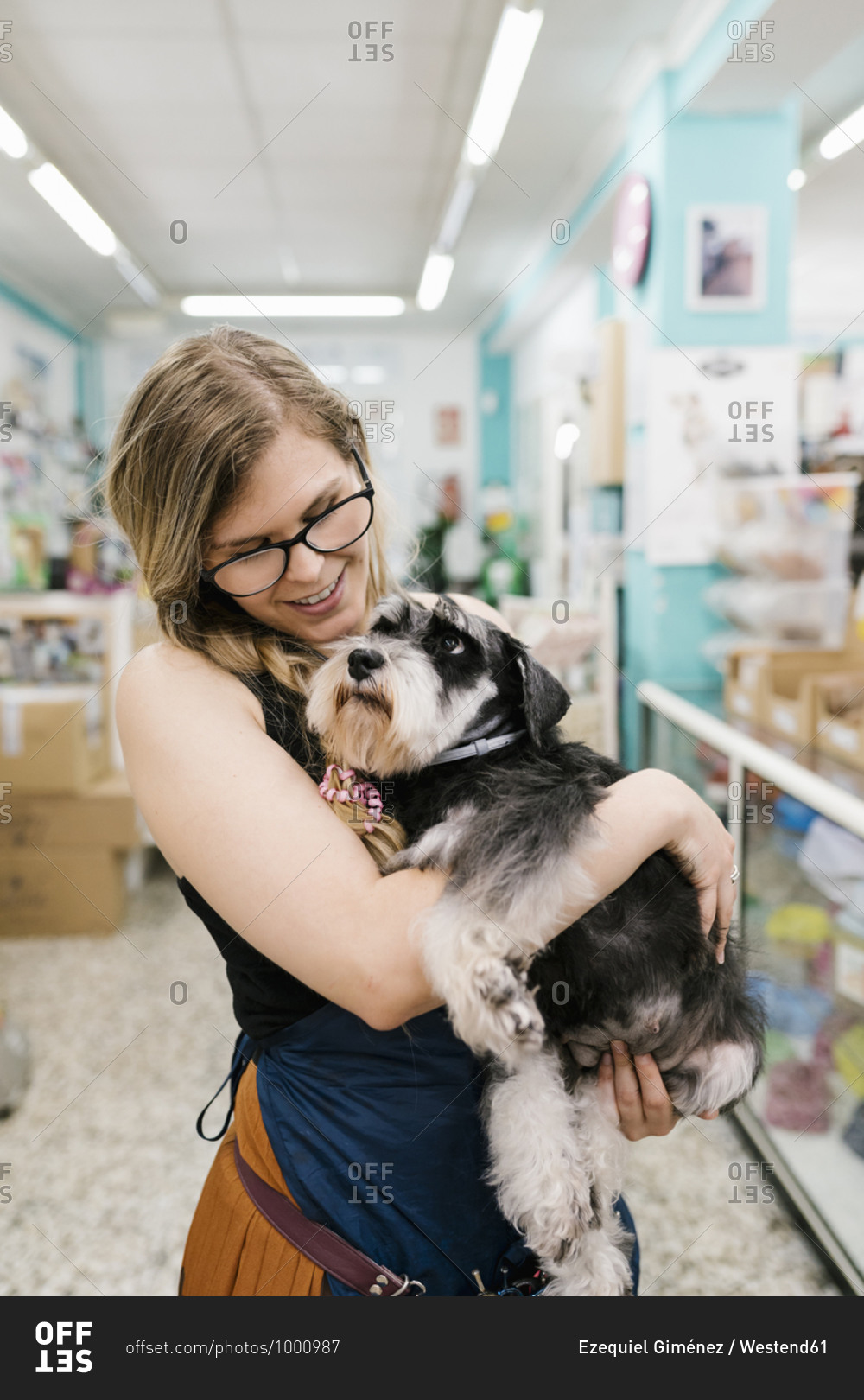 Happy female groomer embracing schnauzer while standing in pet salon