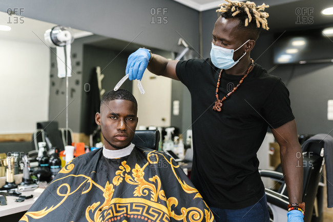 Male hairdresser wearing salon and gloves cutting young man's hair in barber shop