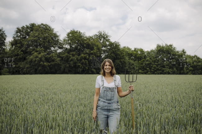 Young woman with hay fork standing in a grain field in the countryside