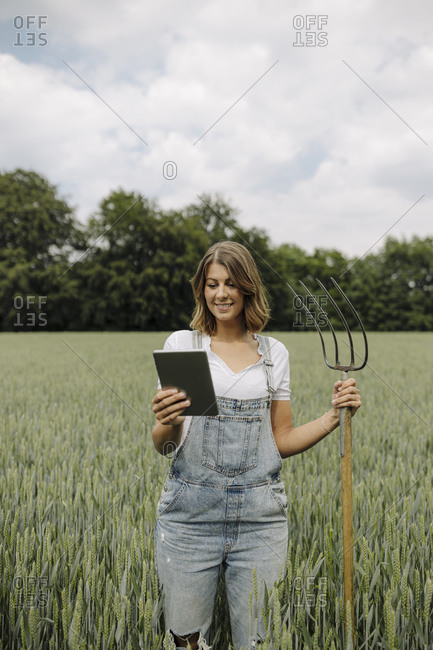 Young woman with hay fork and tablet standing in a grain field in the countryside