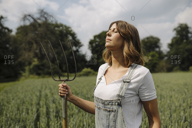 Young woman with hay fork standing in a grain field in the countryside