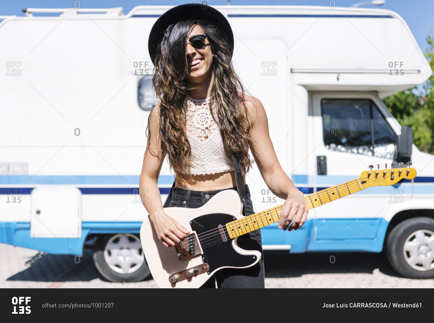 Happy young woman playing electric guitar in front of a camper