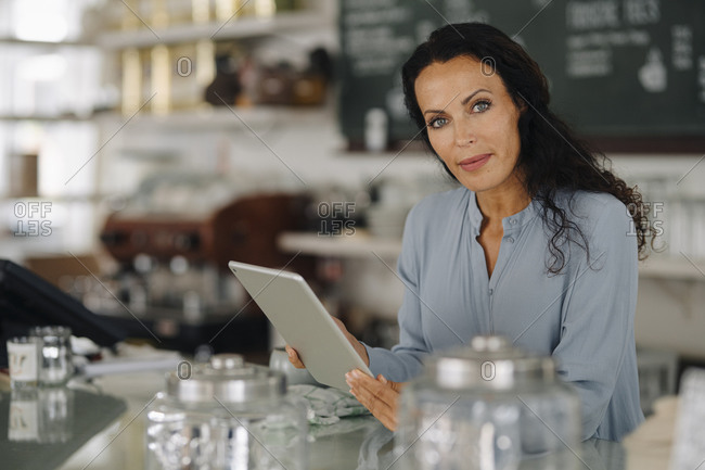 Confident female owner using digital tablet while standing at counter in restaurant