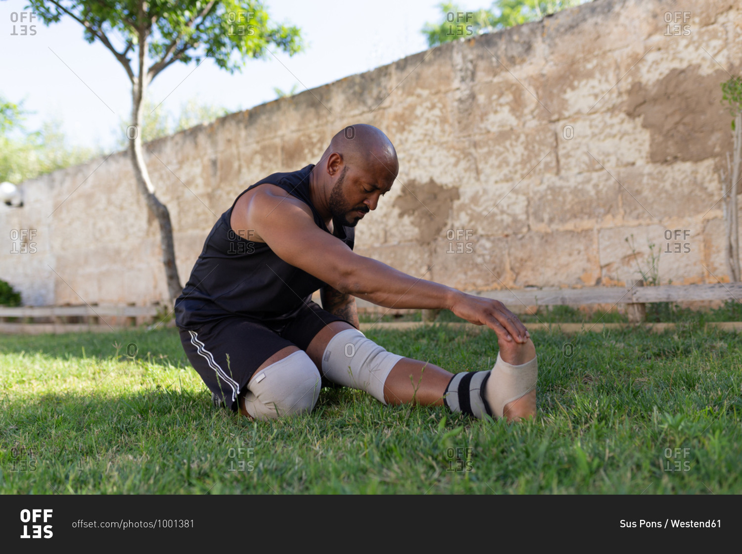 Mature man with shaved head exercising on grassy land against wall in yard