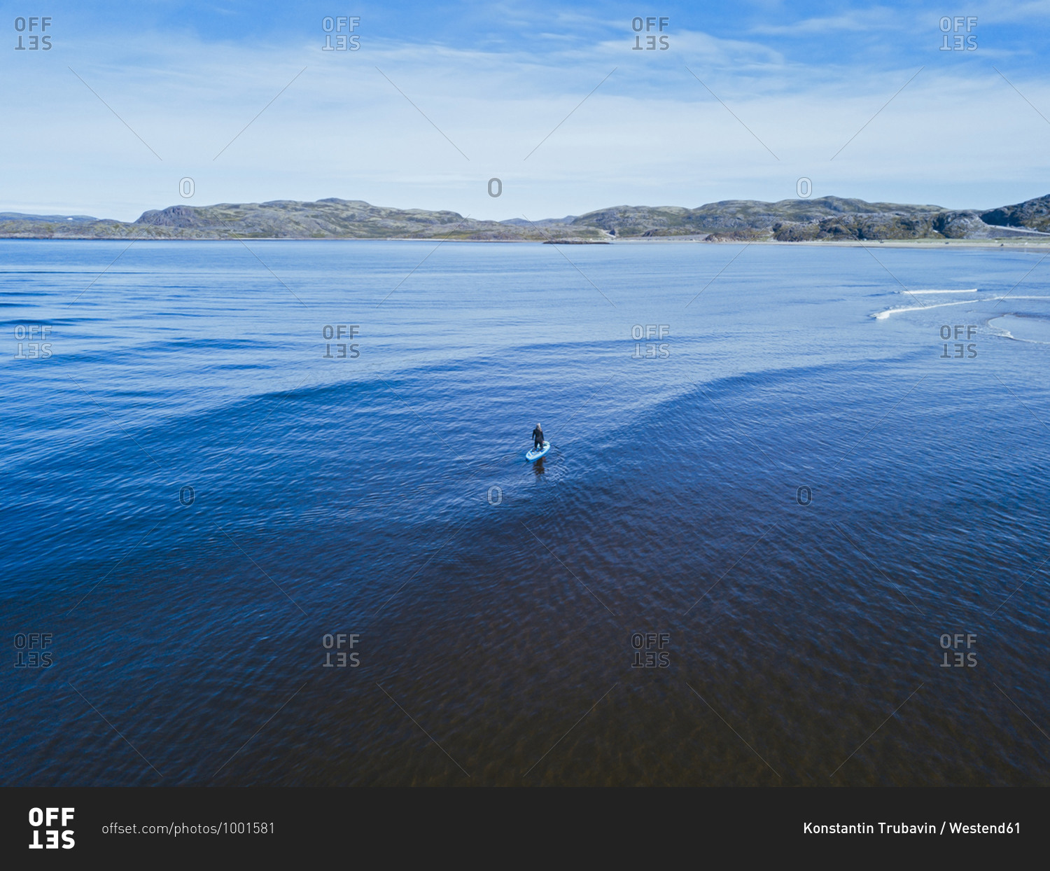 Aerial view of young woman surfing in blue waters of Barents Sea