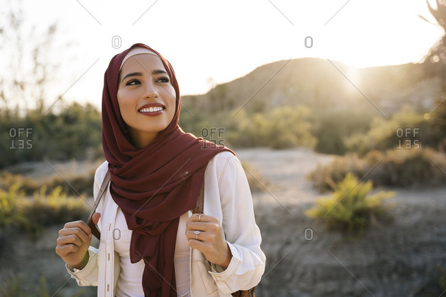 Smiling young tourist woman wearing Hijab in desert landscape looking around