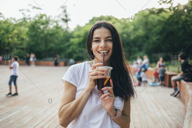 Happy young woman drinking soft drink while standing in park
