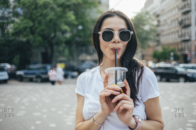 Young woman wearing sunglasses drinking soft drink while standing in city