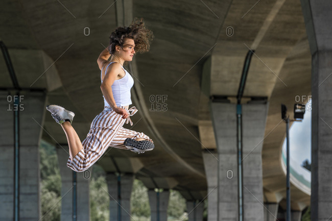 Young woman doing acrobatics and jumping under bridge