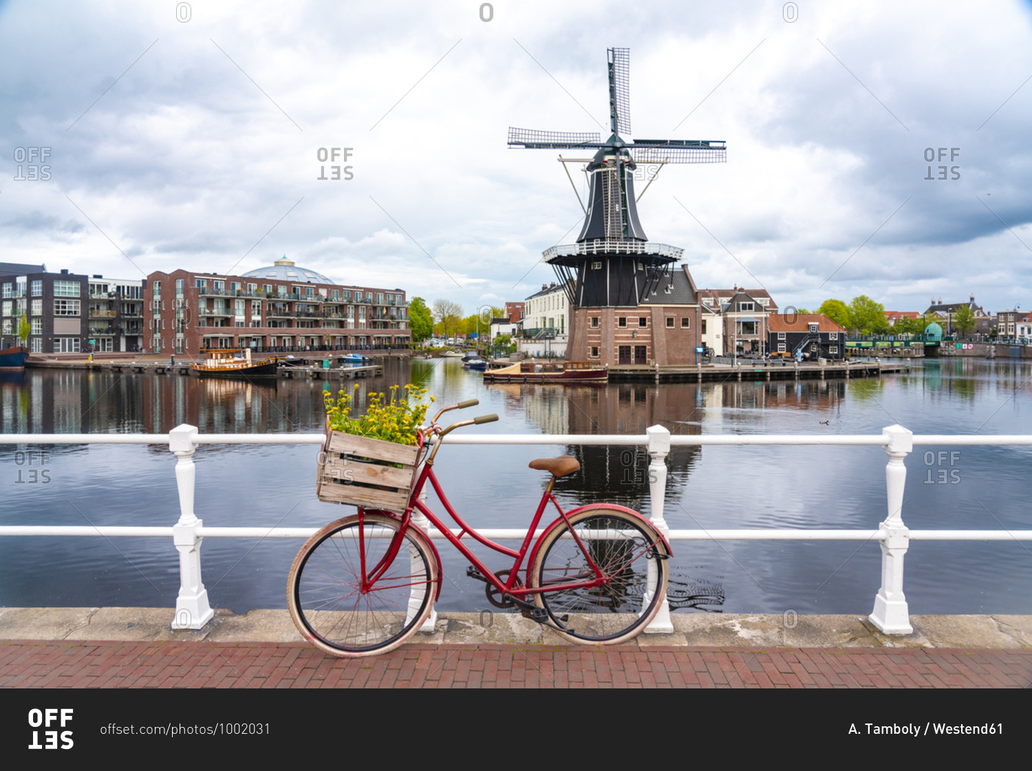 Netherlands- North Holland- Haarlem- Bicycle parked along railing of canal bridge with De Adriaan windmill in background