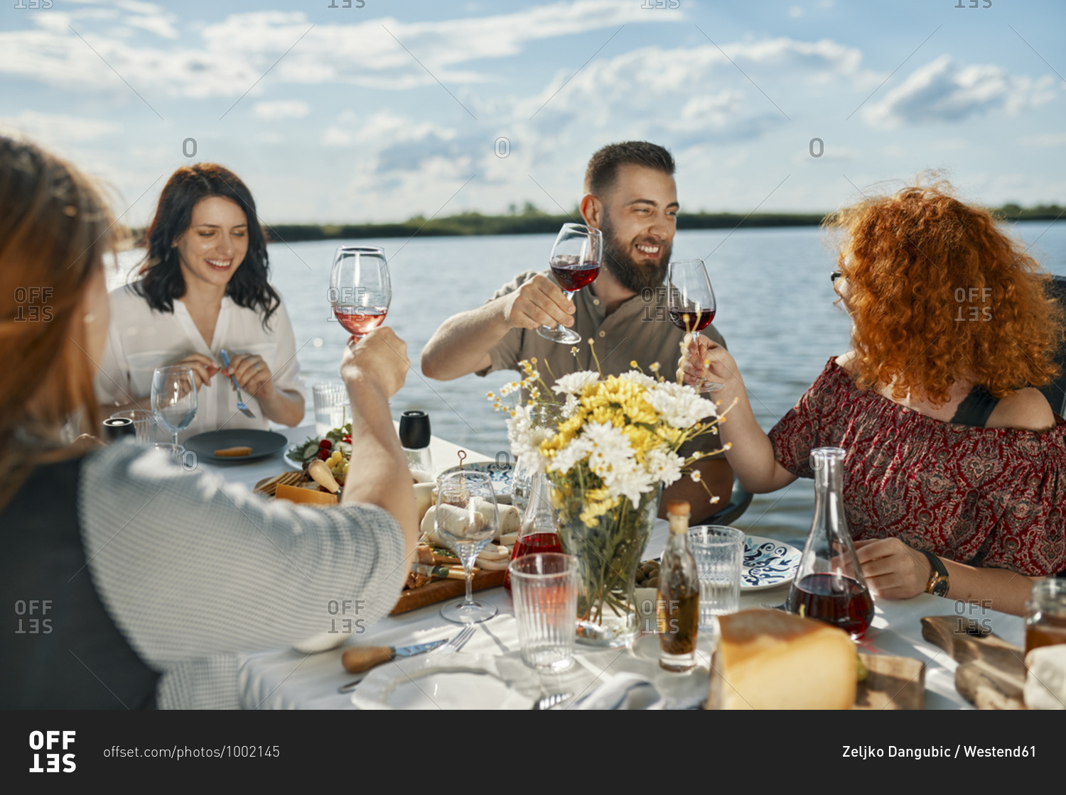 Friends having dinner at a lake raising wine glasses