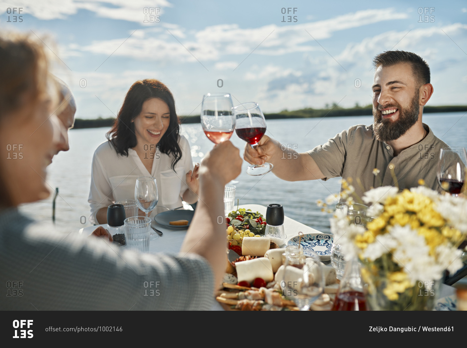 Friends having dinner at a lake clinking wine glasses