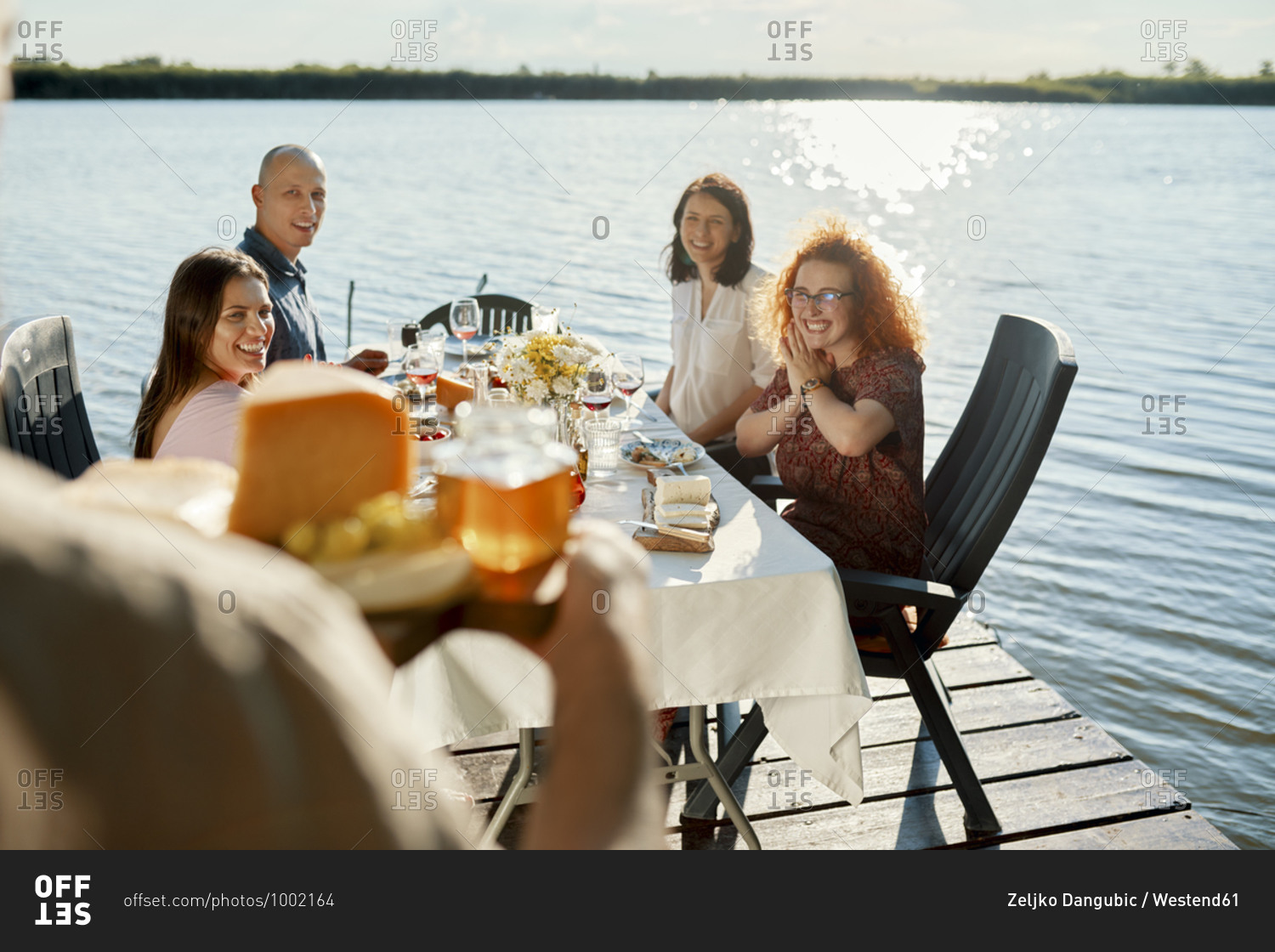 Friends having dinner at a lake with man serving cheese platter