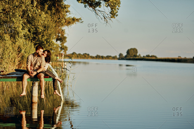 Couple reflected in water sitting on jetty at a lake