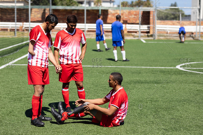 Two multi ethnic teams of male five a side football players wearing a team strip playing a game at a sports field in the sun, player with prosthetic leg sitting player without arm talking to him.